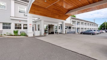 A motel with a covered entrance, a parking lot, and a row of cars parked outside.
