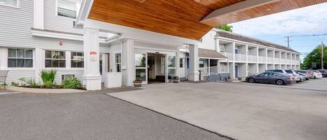 A motel with a covered entrance, a parking lot, and a row of cars parked outside.