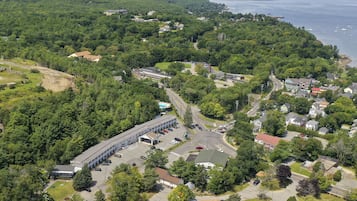 An aerial view of a residential area with a large building complex, surrounded by dense greenery and a coastline.