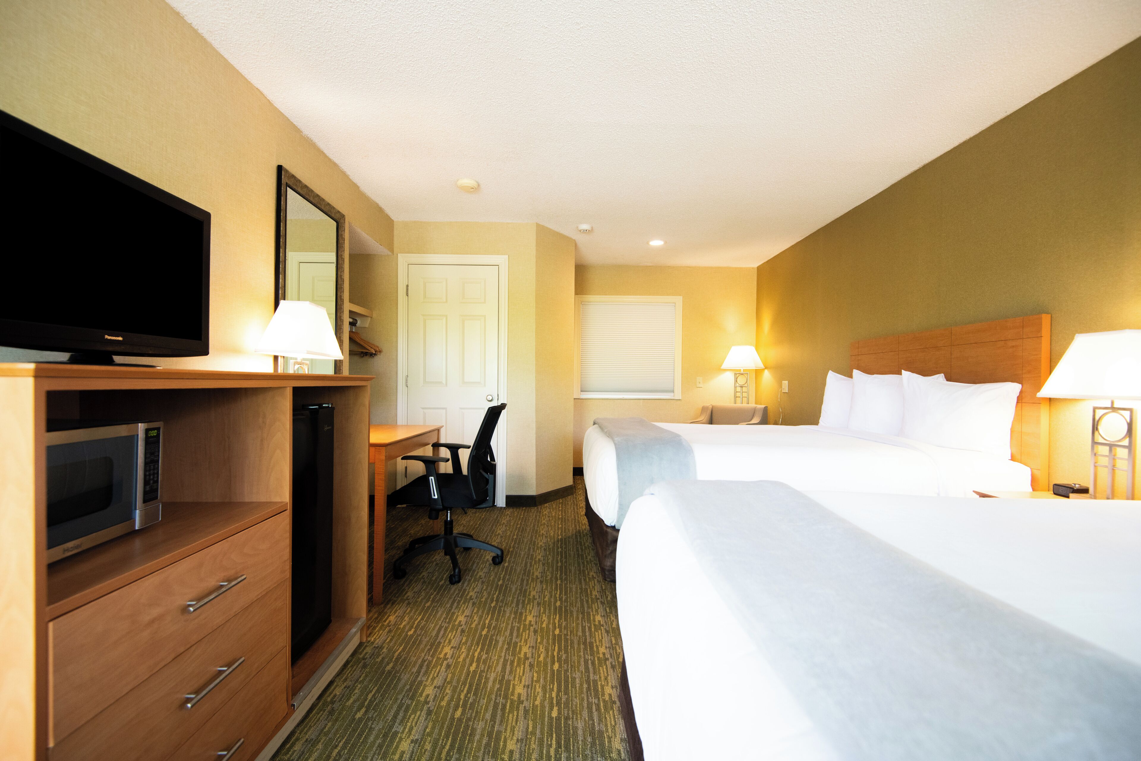 A hotel room with a television, desk, chair, two beds, and lamps.