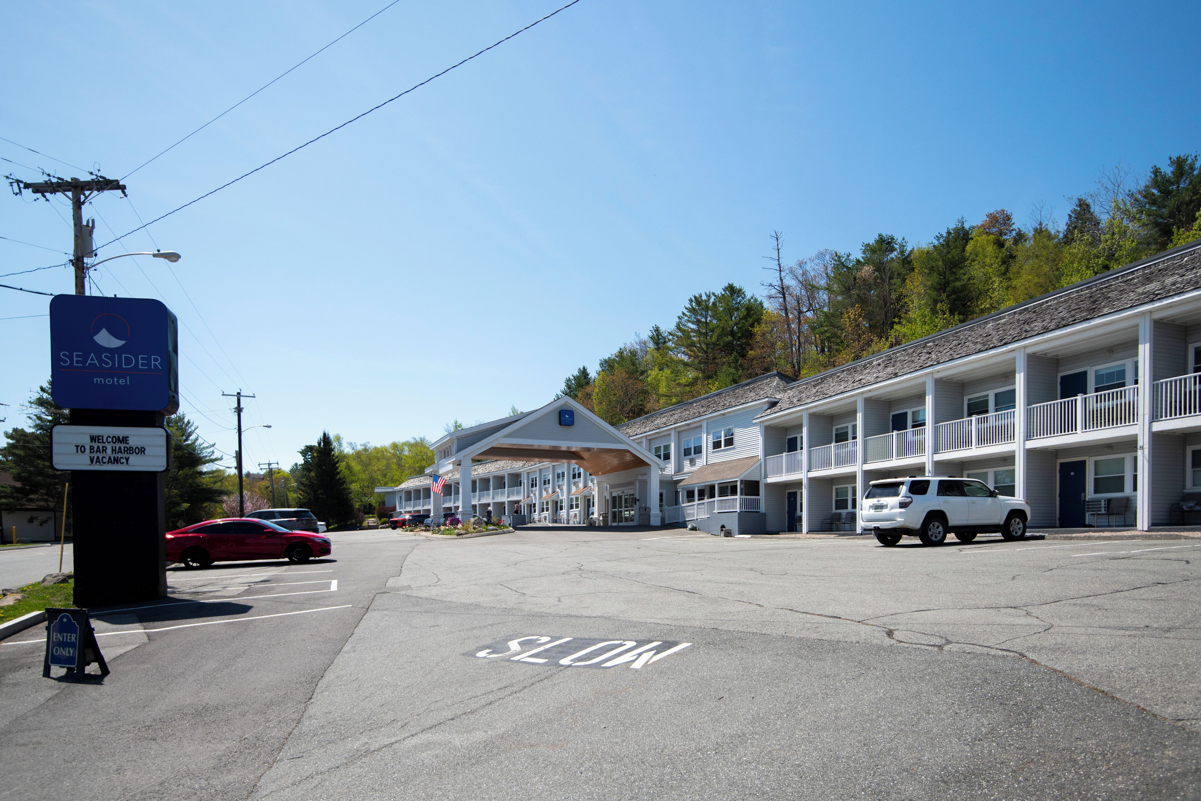 Un motel doté d’une entrée abritée, de plusieurs balcons et d’un panneau indiquant une limitation de vitesse (« RALENTIR ») sur la route.