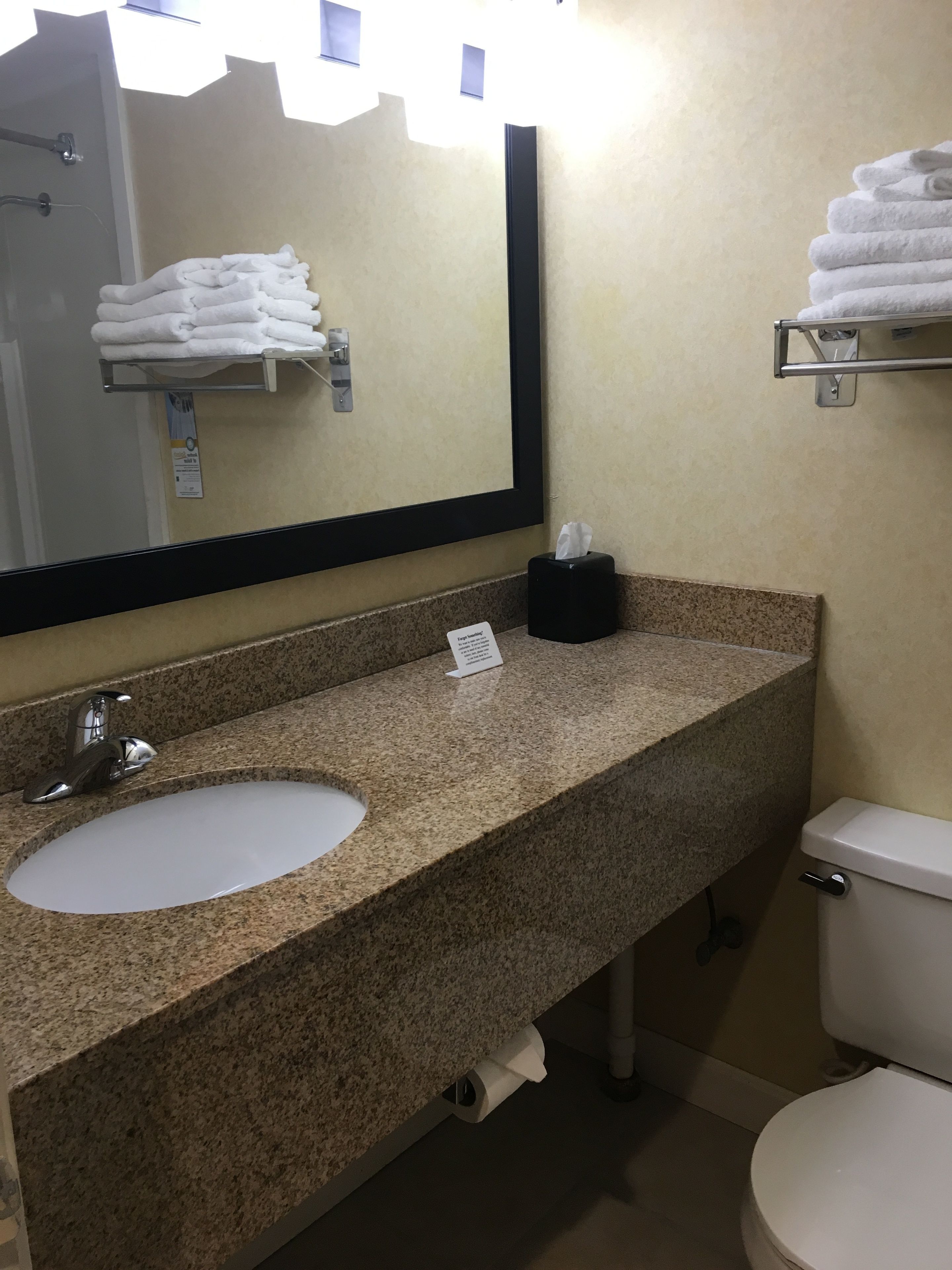 A bathroom with a granite countertop, a white sink, a mirror, a towel rack, and a toilet.