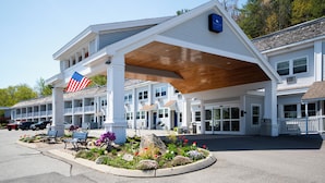 A motel with a covered outdoor area, a flag, and a landscaped garden with benches.