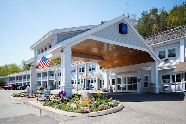 A motel with a covered outdoor area, a flag, and a landscaped garden with benches.