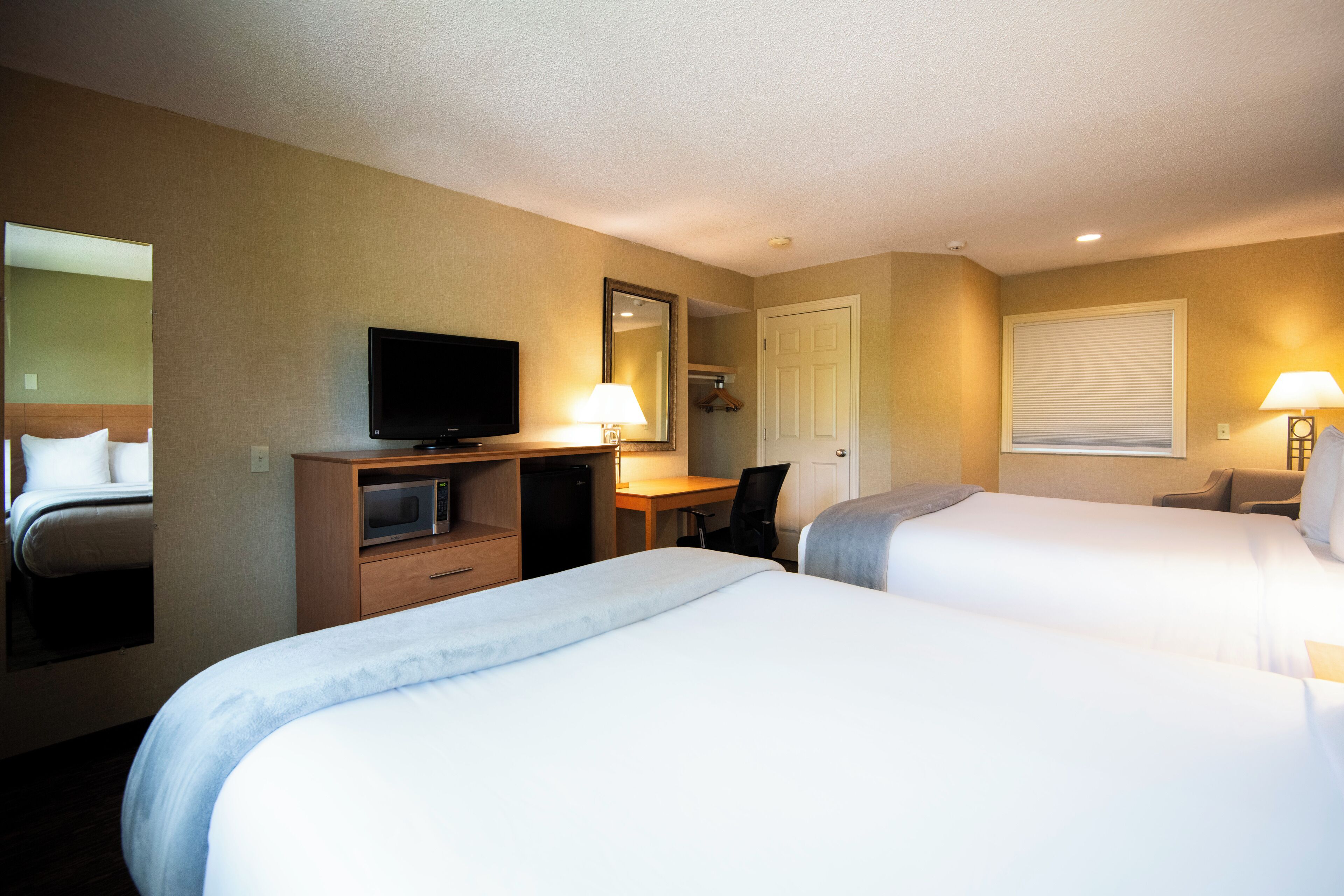 Une chambre d’hôtel avec deux lits, un bureau, une télévision et un miroir.