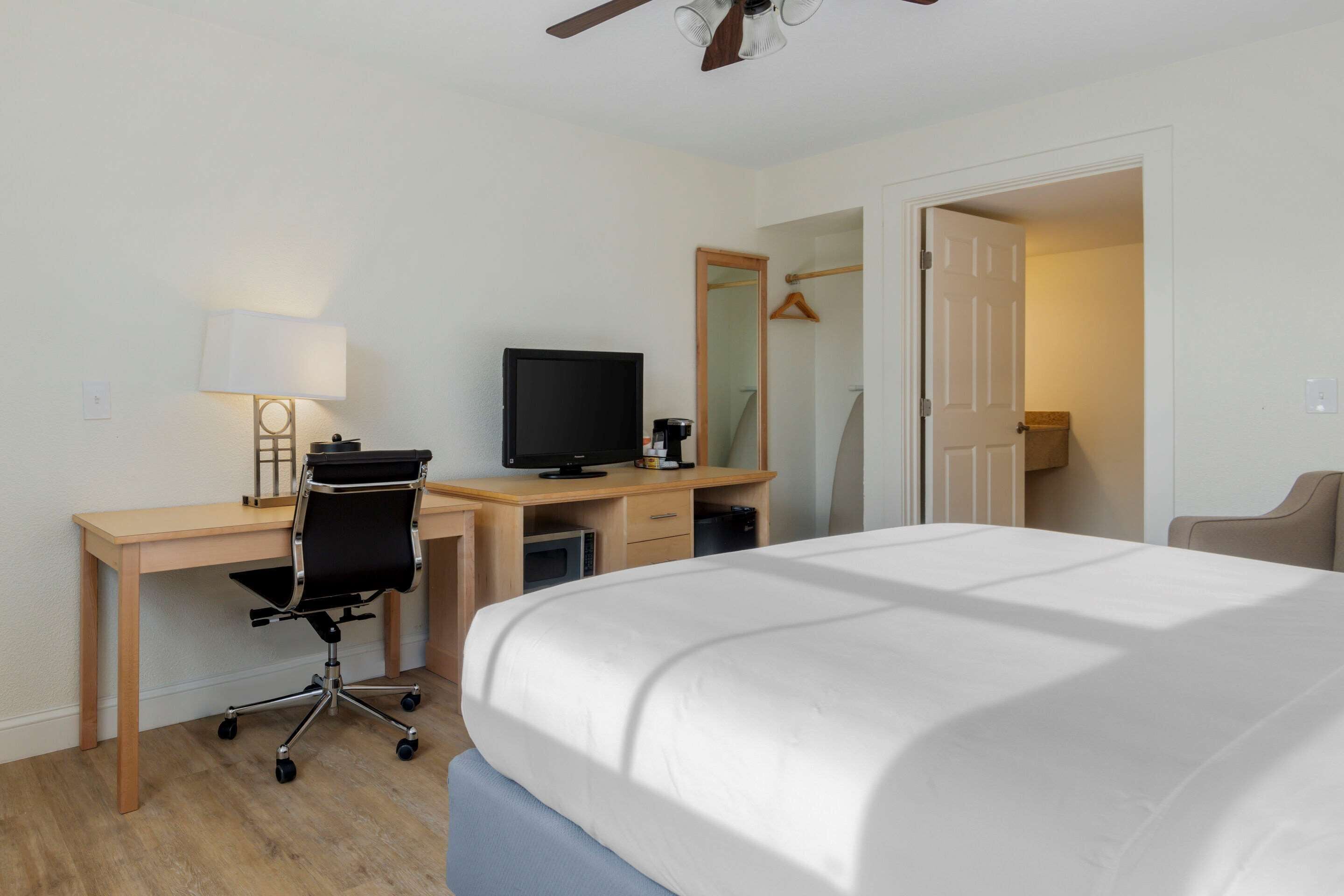 A hotel room with a bed, desk, chair, television, and a mirror.