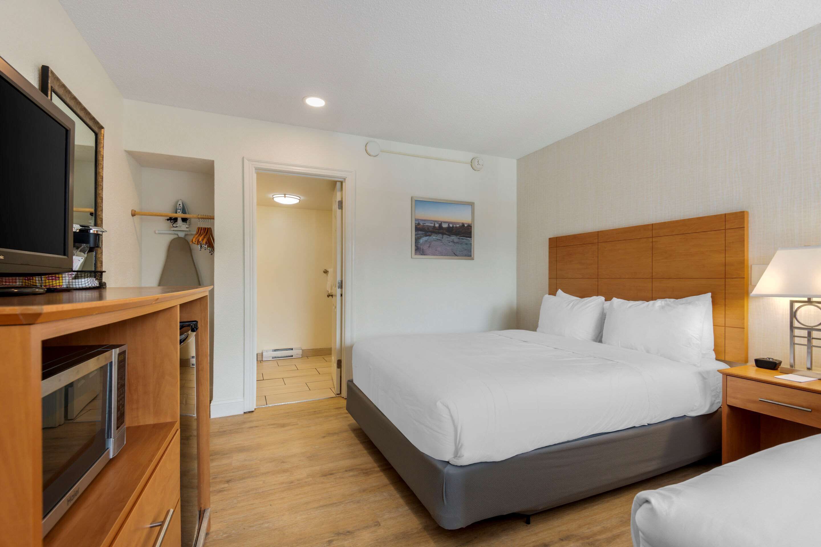 A hotel room with a bed, a TV, a desk with a lamp, and a painting on the wall.