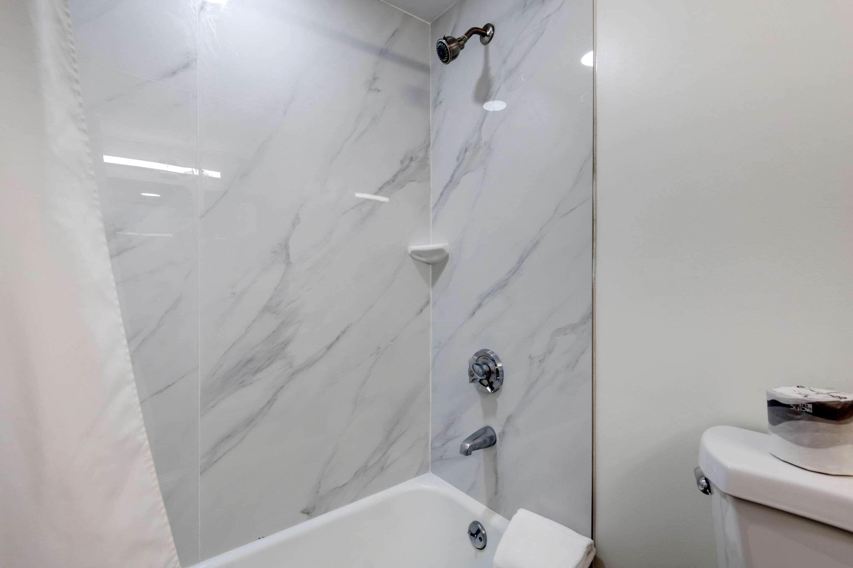 Een badkamer met een witte marmeren wand, een bad en een toilet.