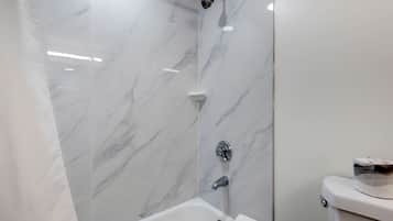 Een badkamer met een witte marmeren wand, een bad en een toilet.