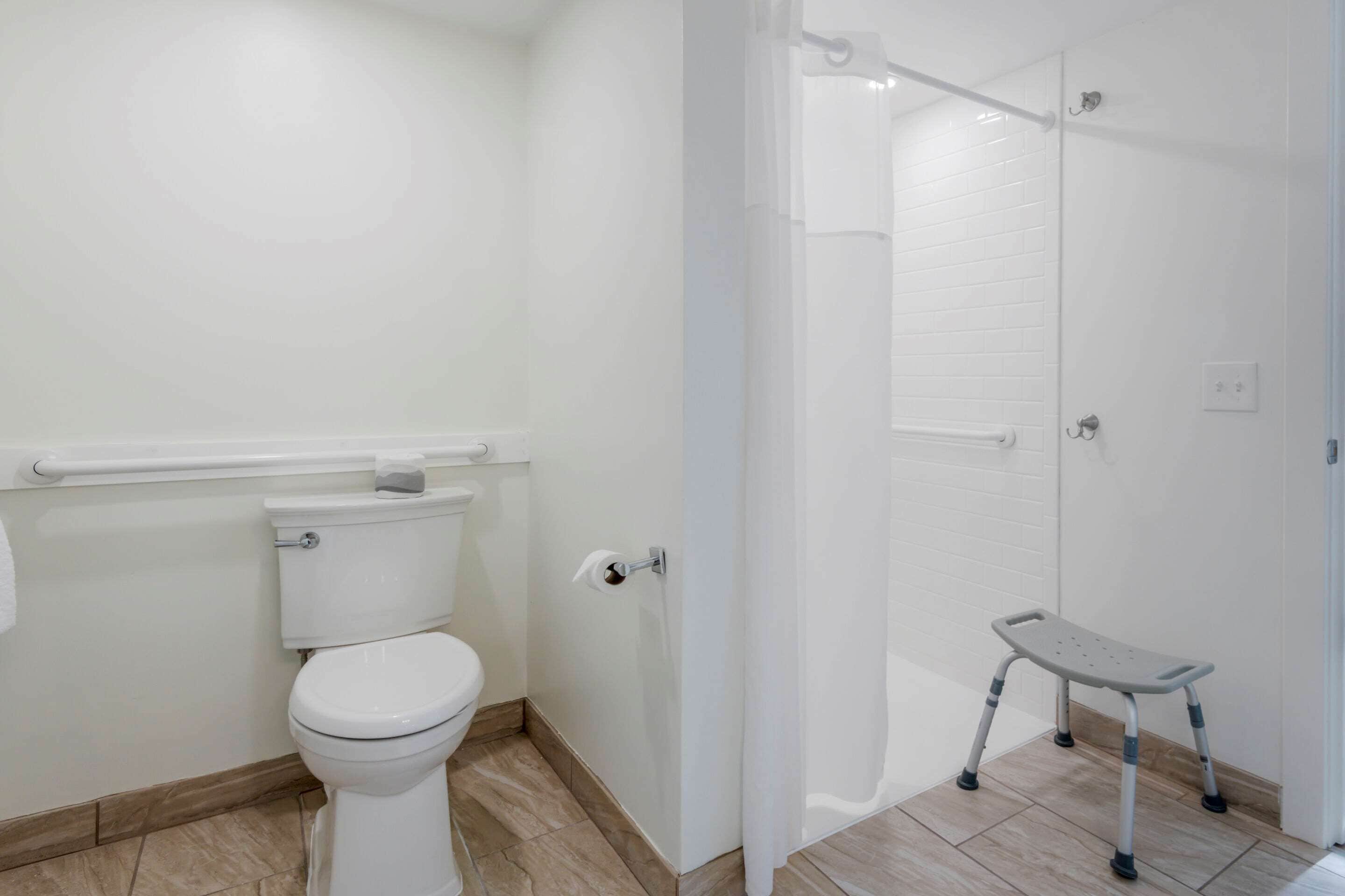 A bathroom with a toilet, a shower with a glass door, and a step stool.