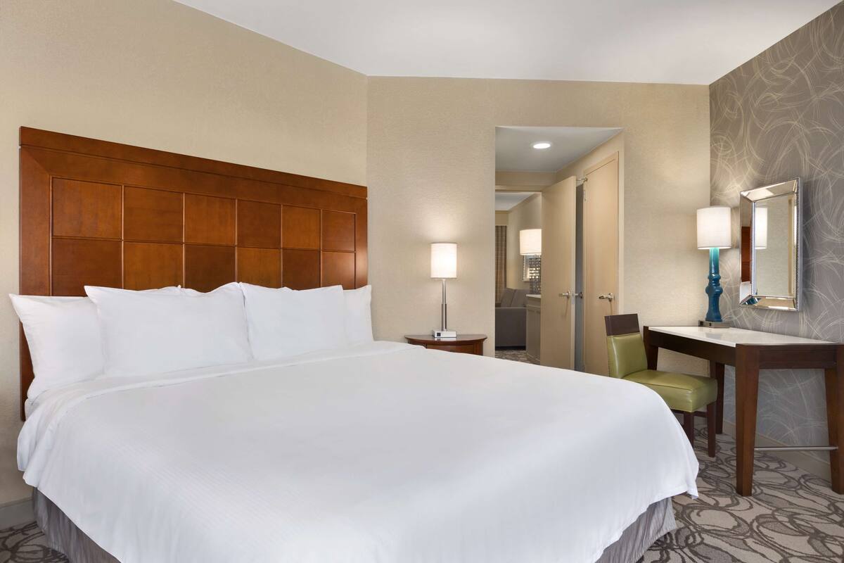 A hotel room with a large bed, a desk, a chair, a mirror, and a lamp.