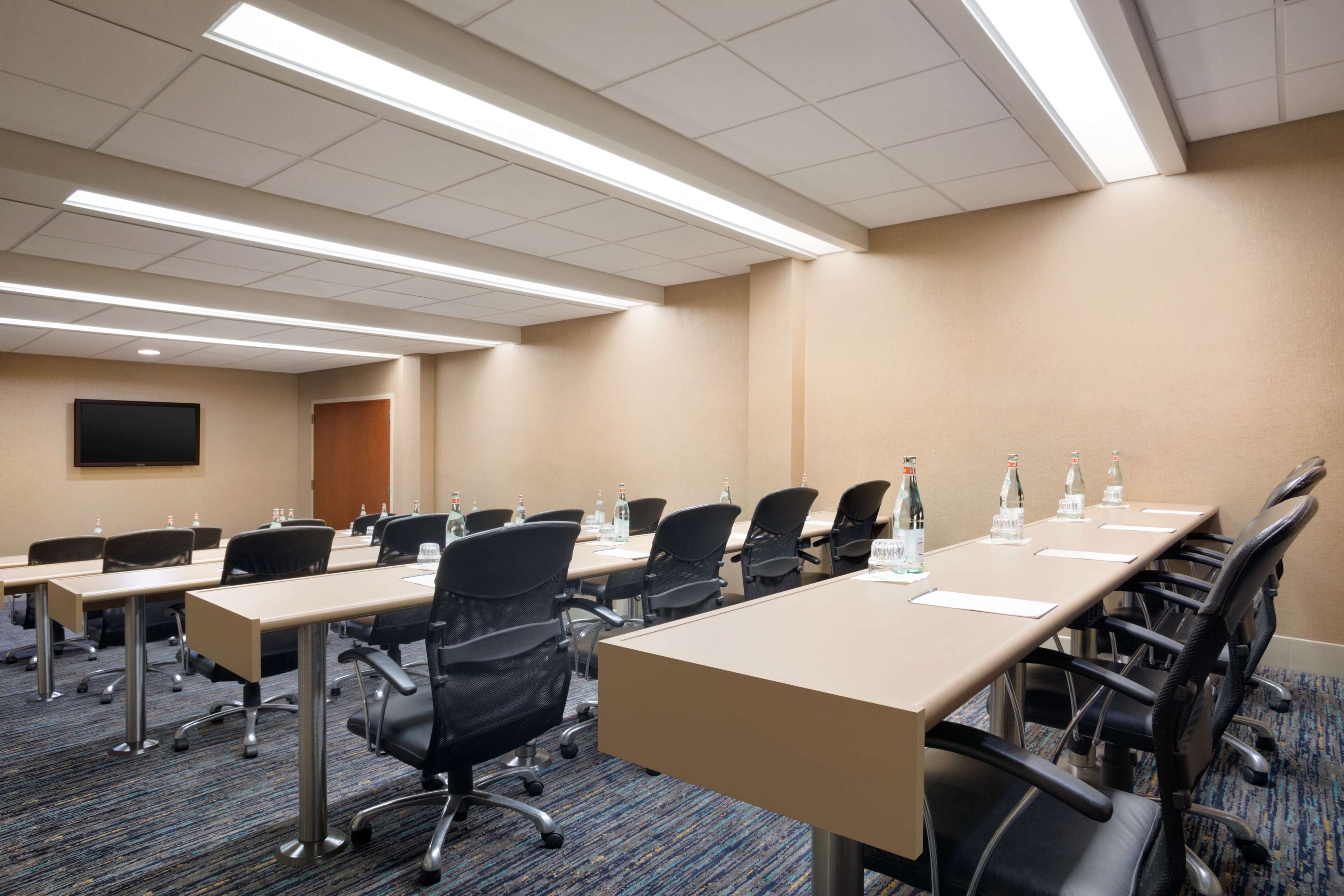 Une salle de conférence avec de longues tables, des chaises et des bouteilles d’eau.