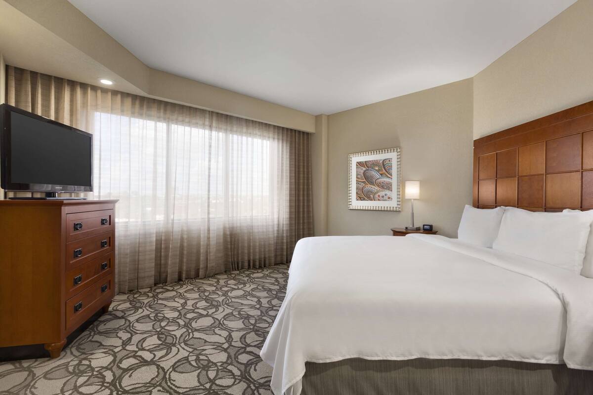 A hotel room with a large bed, a dresser, a flat-screen TV, and a window with curtains.