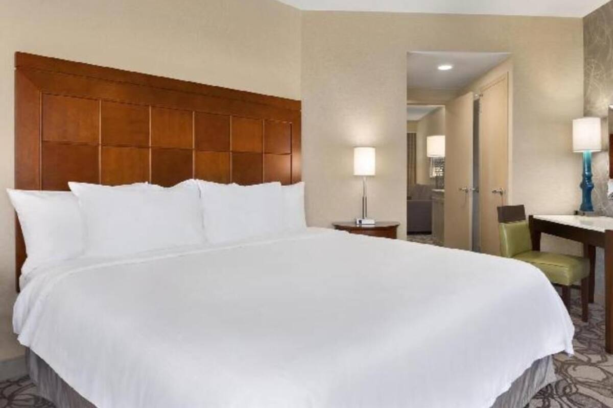 A hotel room with a large bed, a wooden headboard, a desk with a lamp, and a chair.