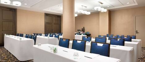 A conference room with tables set up for a meeting, blue chairs, and a large pillar in the center.
