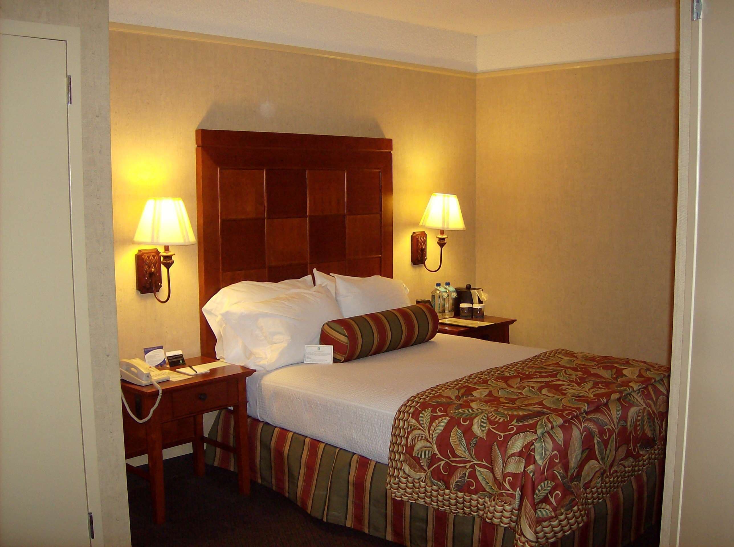 A hotel room with a large bed, two bedside lamps, a wooden nightstand with a telephone, and a patterned bedspread.
