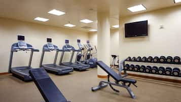 Un gimnasio con cintas de correr, una banca y una estantería con mancuernas.