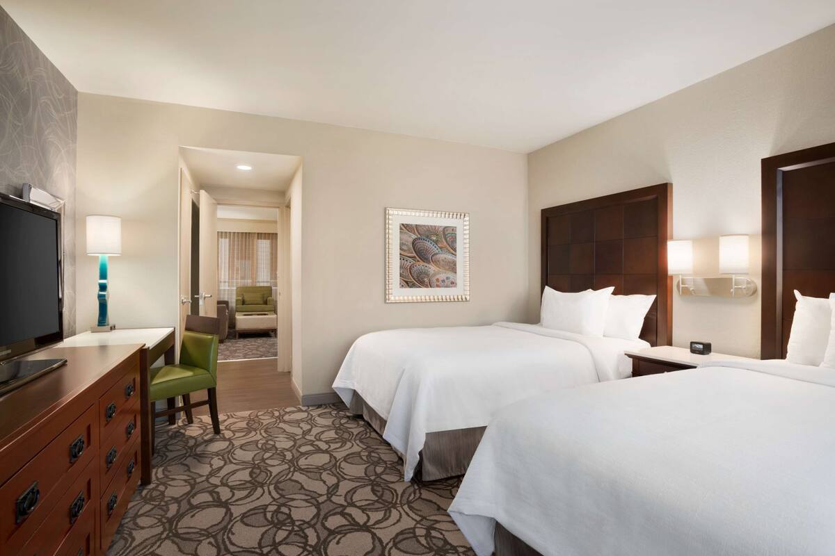 A hotel room with two beds, a desk, a TV, and a chair.