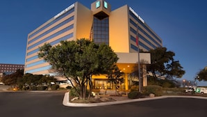 A modern building with "EMBASSY SUITES" signage, featuring a prominent entrance and landscaped surroundings.