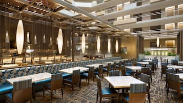 A modern hotel lobby with multiple seating areas, including booths and tables, and a central area with a water feature.