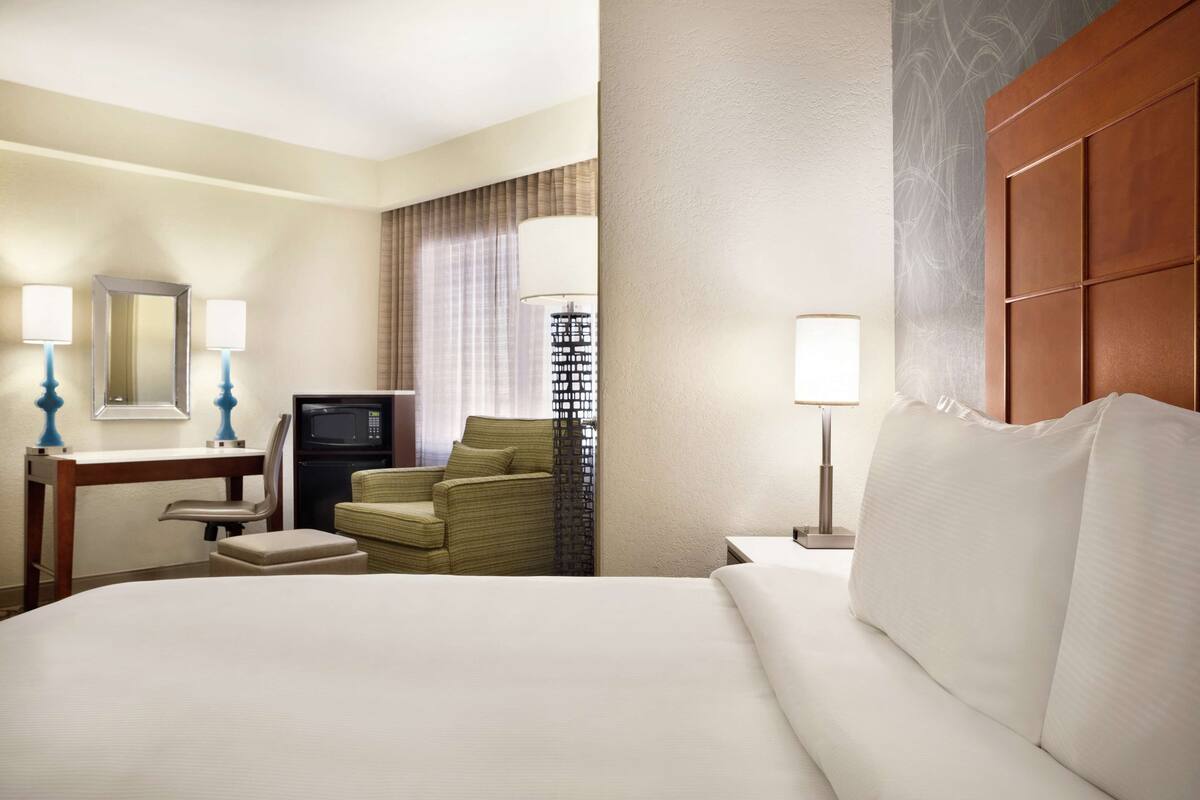 A hotel room with a bed, a desk with a chair, a television, and a lamp.