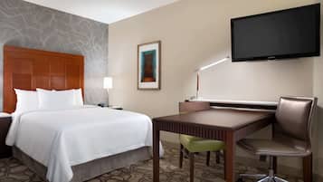 A hotel room with a bed, desk, chair, television, and artwork on the wall.