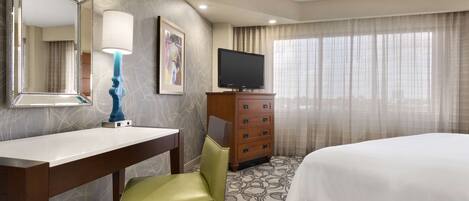 A hotel room with a bed, a desk with a chair, a dresser, a television, and a large mirror.