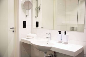 Un bagno moderno con un lavandino bianco, due asciugamani ad aria, uno specchio e un box doccia in vetro.