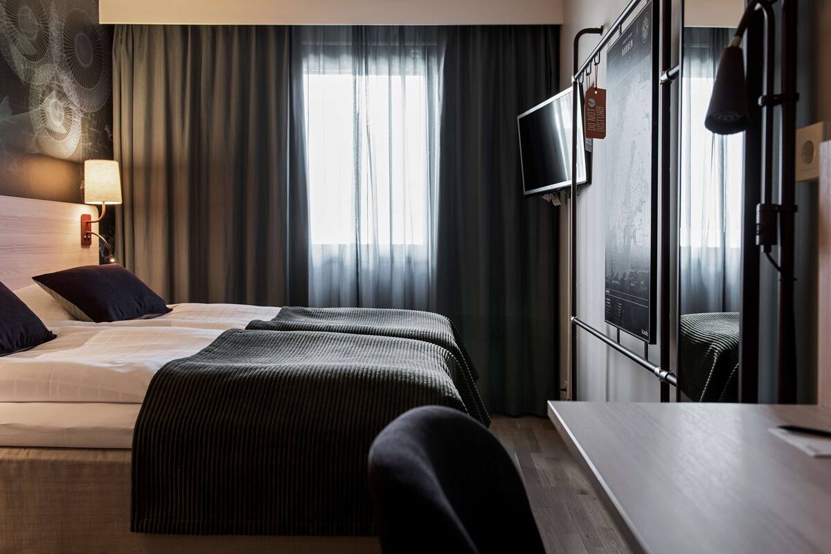 A hotel room with a bed, a desk, a chair, a TV, and a window with curtains.