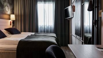 Habitación de hotel con cama, escritorio, silla, televisor y ventana con cortinas.