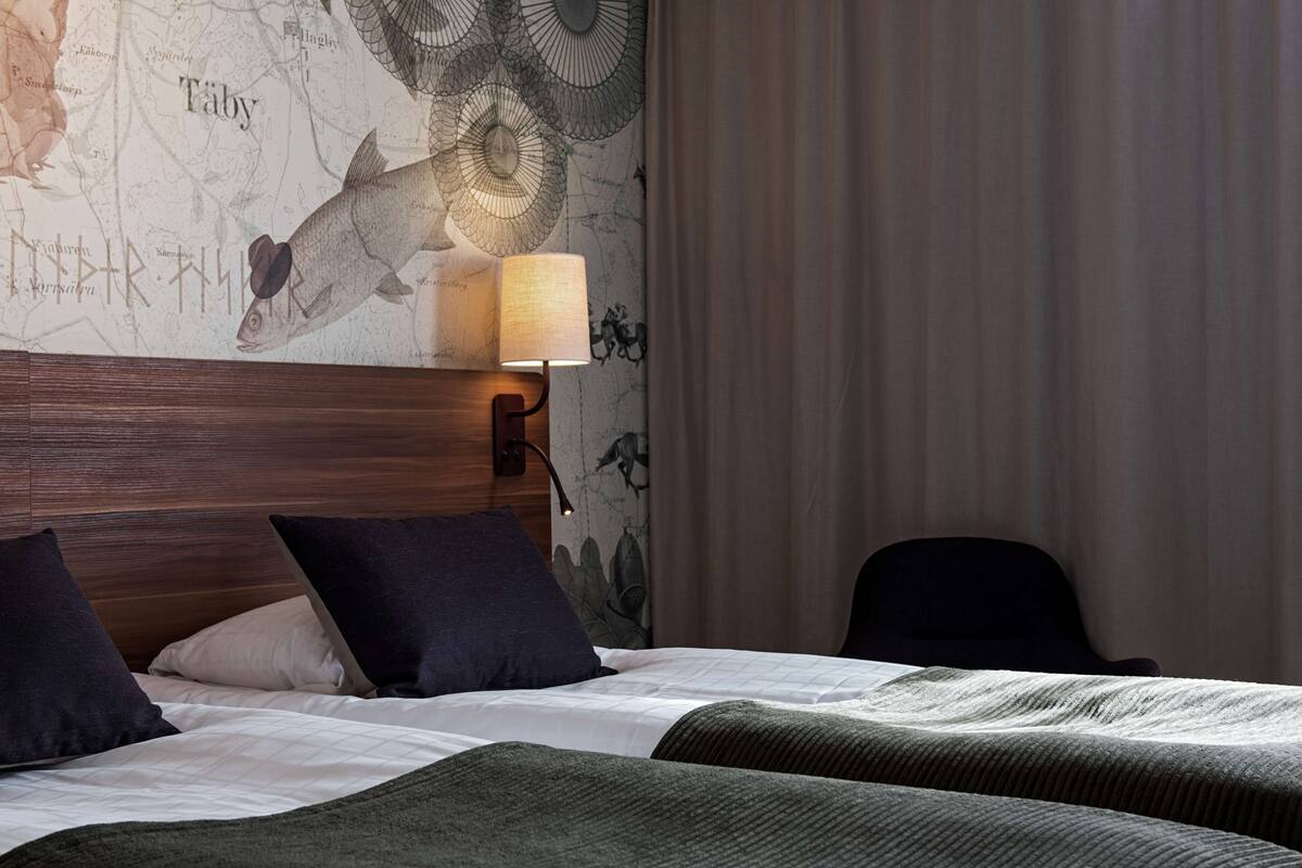 A hotel room with a large bed, two pillows, a headboard, a wall map, a lamp, and a chair.
