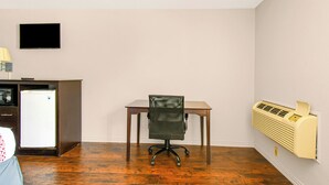 A room with a desk, chair, wall-mounted TV, and an air conditioner.