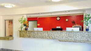 A reception area with a red wall, a clock, a computer, and a plant.