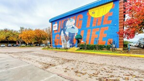 A building with a mural on the side, a parking lot, and autumn trees.