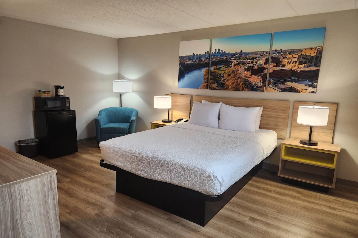 Ein Hotelzimmer mit einem großen Bett, zwei Nachttischen, einem Sessel, einem Schreibtisch und einem Stadtbild an der Wand.