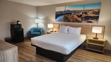 Ett hotellrum med en stor säng, två sängbord, en stol, ett skrivbord och en tavla med en stadsbild på väggen.