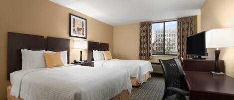 A hotel room with two beds, a desk, a chair, a TV, and a window with curtains.