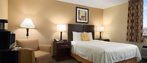 A hotel room with a bed, a chair, a desk with a lamp, a television, and a framed picture on the wall.