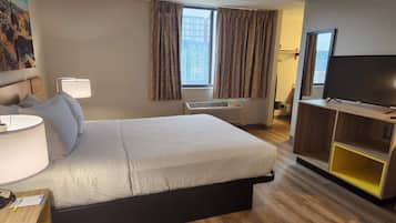 A hotel room with a bed, a desk with a lamp, a TV, and a window with curtains.