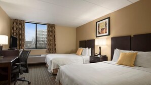 Une chambre d’hôtel avec deux lits, un bureau, une chaise, une télévision et une fenêtre avec des rideaux.
