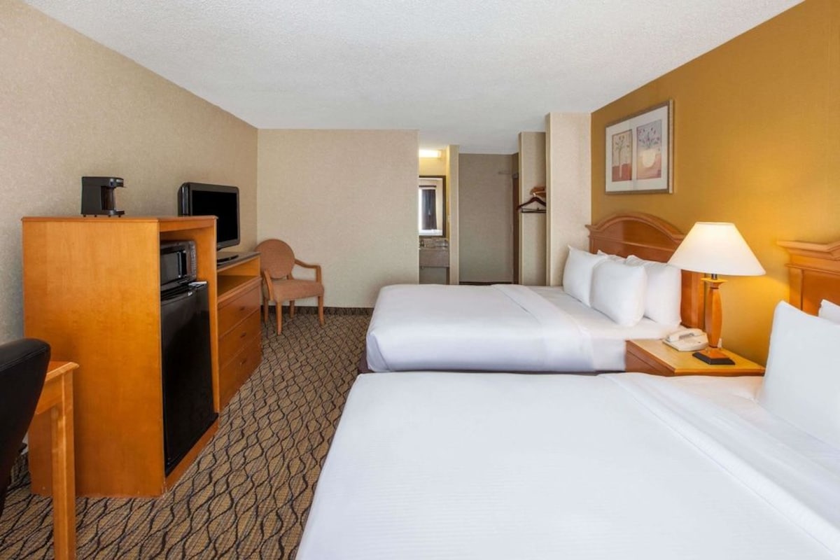 Una habitación de hotel con dos camas, un escritorio con computadora, una silla y un televisor.