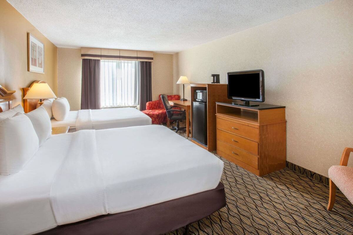 A hotel room with two beds, a desk, a television, a microwave, and a chair.