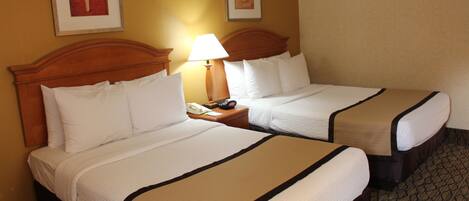 Two adjacent hotel beds with white bedding and brown headboards, a bedside table with a lamp, and two framed floral artworks on the wall.