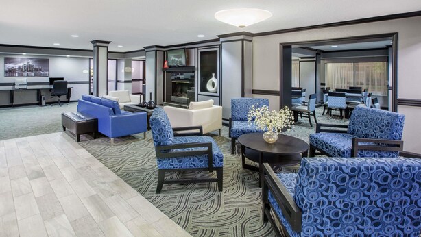 A modern hotel lobby with a reception desk, seating area with blue patterned chairs, a fireplace, and a large mirror reflecting the room. - Americas Best Value Inn Canton (Canton)