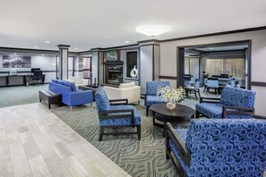 A modern hotel lobby with a reception desk, seating area with blue patterned chairs, a fireplace, and a large mirror reflecting the room. - Americas Best Value Inn Canton (Canton)