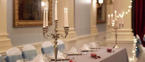 A long dining table with white tablecloths, candles, and blue and white napkins.