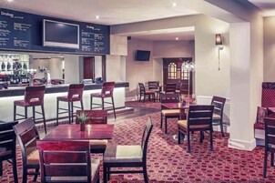 Un restaurante con barra, varias mesas y sillas, y una alfombra estampada.