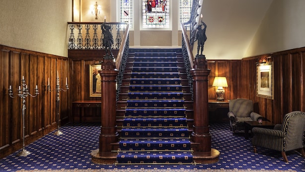 Un magnifique escalier orné de balustrades travaillées, un tapis à motifs et une fenêtre à vitraux au-dessus.