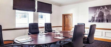 A conference room with a large table, black chairs, and a patterned carpet.