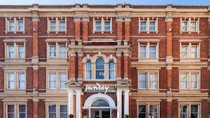 Un grand bâtiment en briques avec une entrée centrale, de nombreuses fenêtres et une enseigne indiquant « Sunday Hotel ».